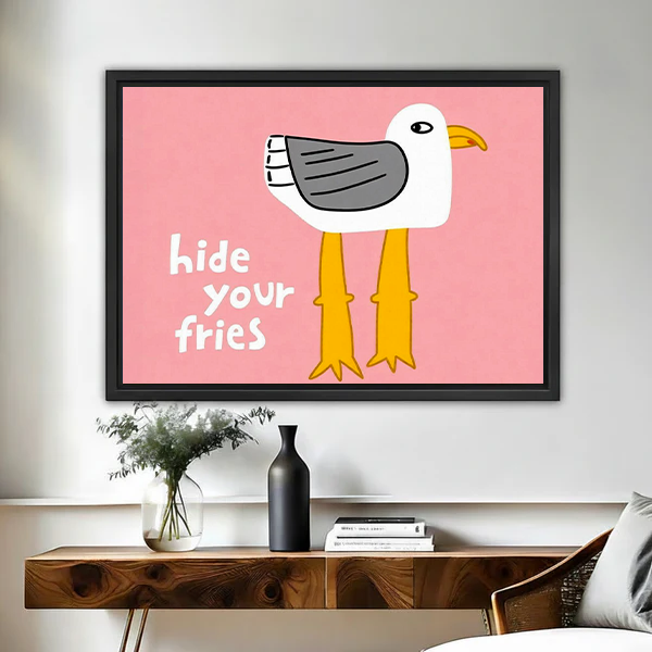Black-framed Hide Your Fries seagull canvas wall art on pink above a wooden console with vases.