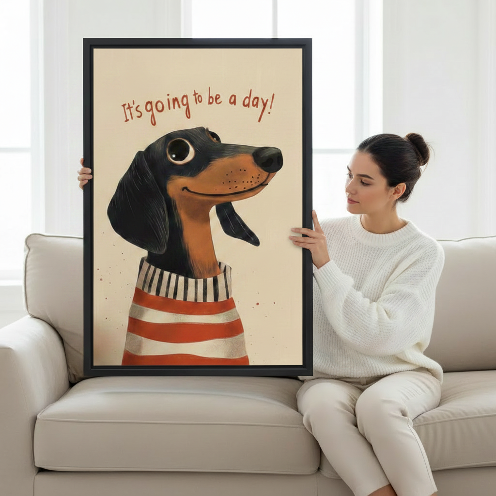 Woman sitting on a cream sofa holding a large black-framed canvas print of a cheerful dachshund in a striped sweater with the humorous quote It's Going to Be a Day on a beige background