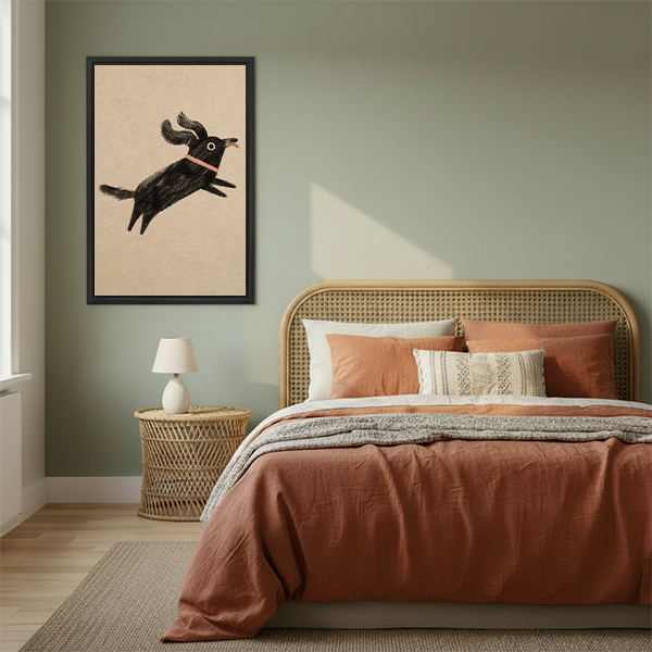 Framed whimsical jumping black dog wall art displayed in cozy bedroom with sage green walls and terracotta bedding