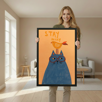 Woman holding framed whimsical cat and bird canvas wall art in a softly lit living room.