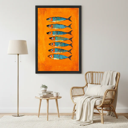 Orange Turquoise Sardines artwork in a black frame beside a lamp and pale rattan chair.