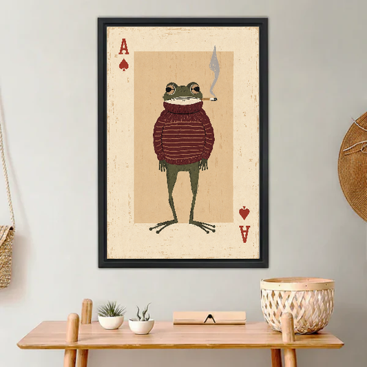 whimsical frog card canvas wall art framed above a light wood console with cacti and basket.
