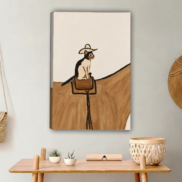 cowboy saddle cat canvas wall art unframed above a light wood console with cacti and basket.