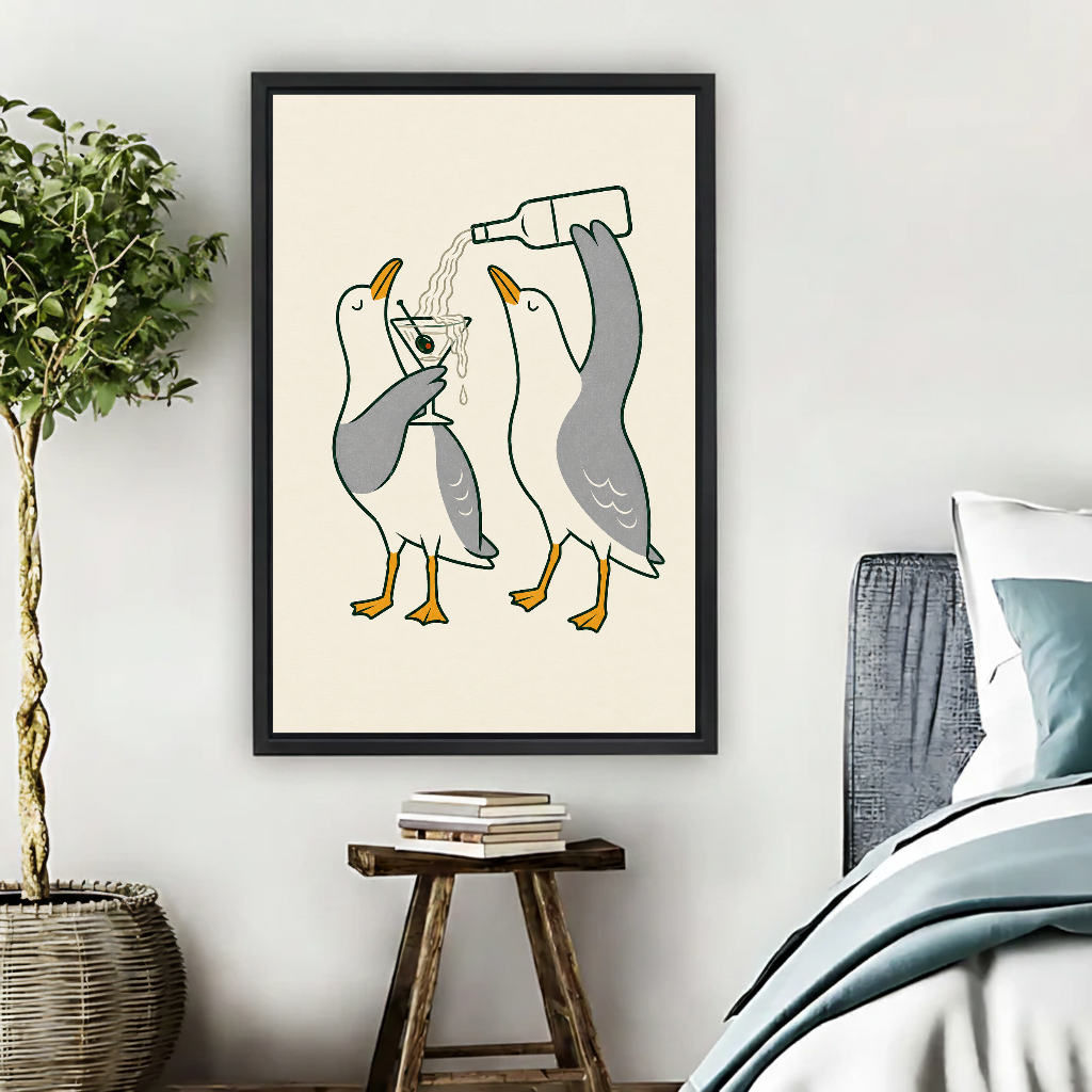 Martini Pouring Seagull Pair canvas art framed beside a bed with muted blue bedding and a potted tree.