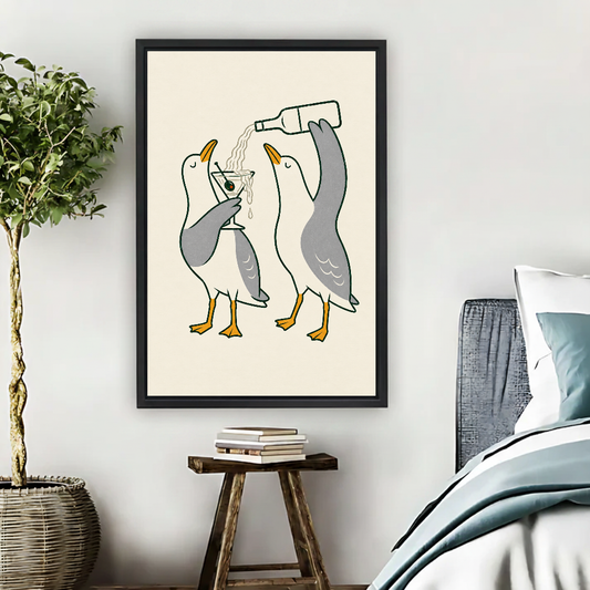 Martini Pouring Seagull Pair canvas art framed beside a bed with muted blue bedding and a potted tree.