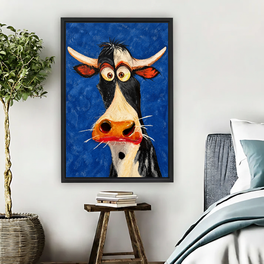 Funny Cow Canvas Wall Art framed beside blue bedding, a leafy plant, and books.