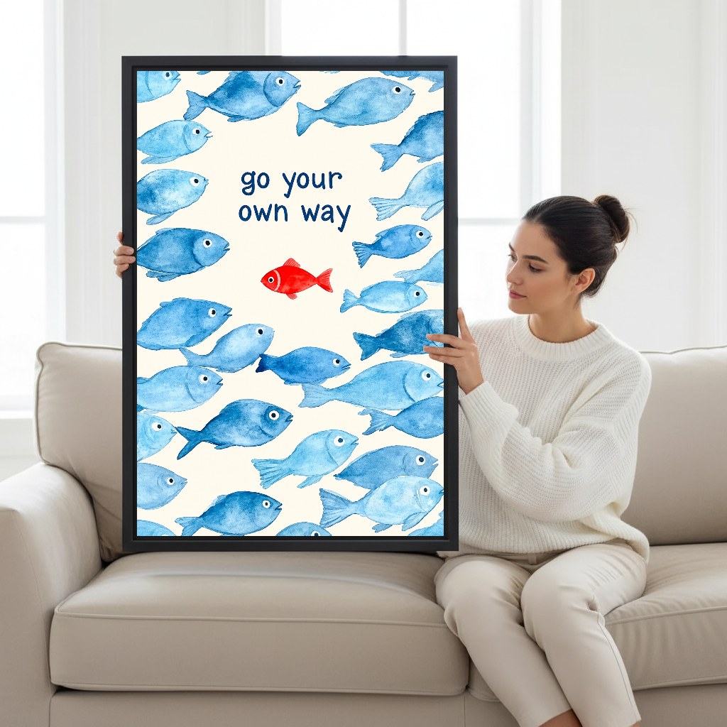 Go Your Way Fish Canvas Wall Art held in a black frame by a woman seated on a pale sofa.