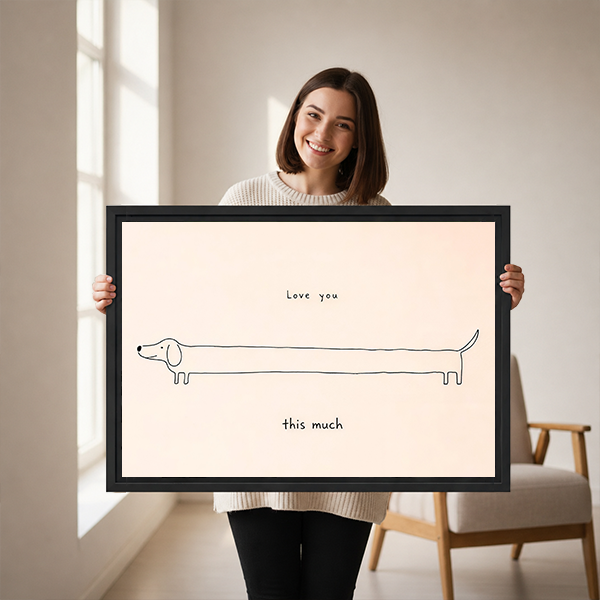 Woman holding framed love you this much dachshund canvas wall art with delicate dog linework on a cream background.