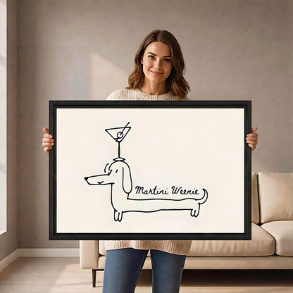 Woman holding a large framed Martini Weenie dachshund minimalist line art print in front of a beige sofa, showing print scale and black frame detail