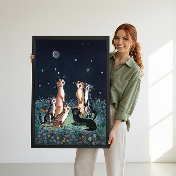 Woman holding black framed whimsical moonlit cats canvas wall art with six felines among flowers and stars.