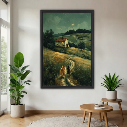 Large black framed print featuring two cats strolling toward a rustic farmhouse at night under a crescent moon, hung in a minimalist hallway with indoor tropical plants