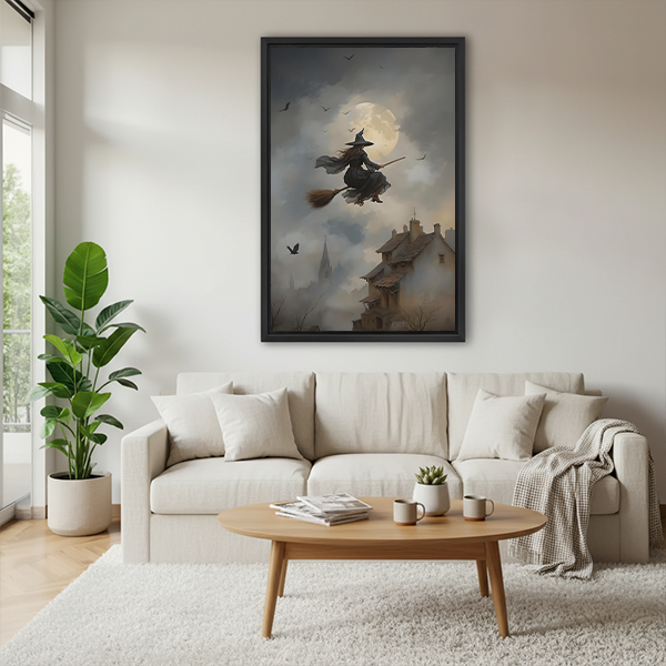 Woman holding black-framed moonlit flying witch canvas wall art featuring a full moon, flying silhouettes, and crooked rooftops.