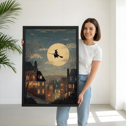 Woman holding black-framed moonlit witch canvas wall art showing a flying witch above a village with glowing windows.