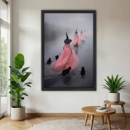 Woman holding framed canvas of three pink-gowned witches in black hats walking through fog with black cats