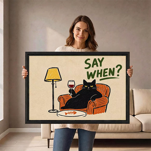 Woman holding framed retro black cat wine canvas wall art with a black cat toasting in an orange armchair.