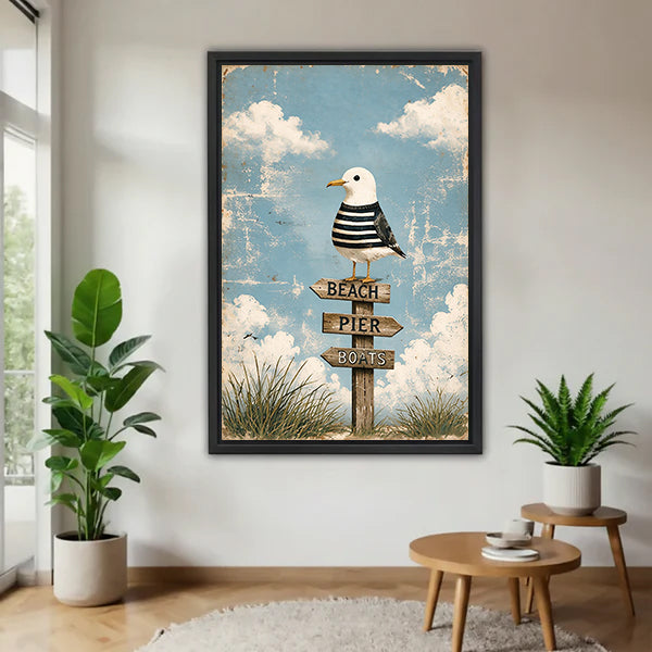 Black-framed coastal seagull signpost canvas wall art on a white wall beside plants