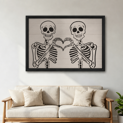 Two skeletons making a heart shape with their bone hands on shiplap background framed canvas above cream linen sofa with white cushions and green plant