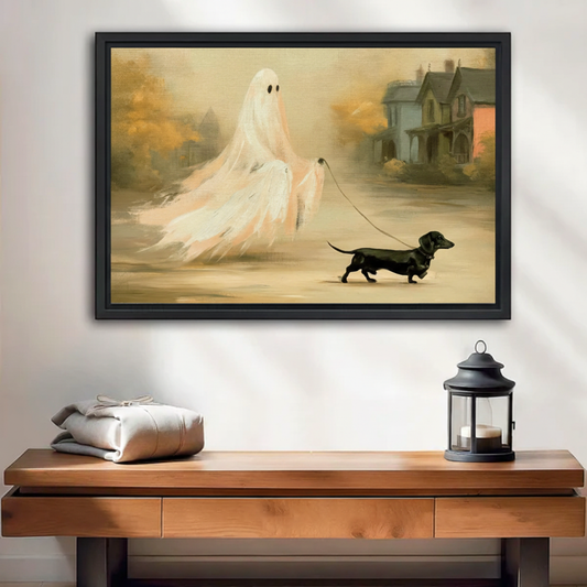 Charming Halloween ghost with black eyes walking a dachshund on leash past misty old houses framed canvas print above a warm walnut console table with lantern and linen parcel