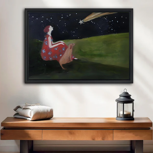 Framed stargazing wall art of a girl in a red floral dress and a deer watching a shooting star on a dark hillside, hung above a wooden console table