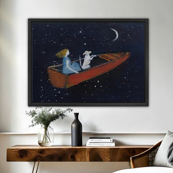 Dreamy starry night framed wall art print of a girl and white dog rowing a red boat under a crescent moon, hung above a wooden console table