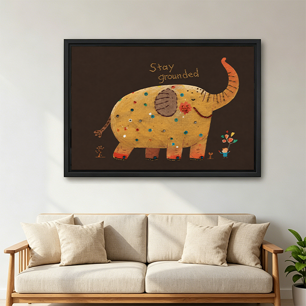 Black framed Stay Grounded elephant canvas wall art above a wooden console with folded blankets and a lantern.