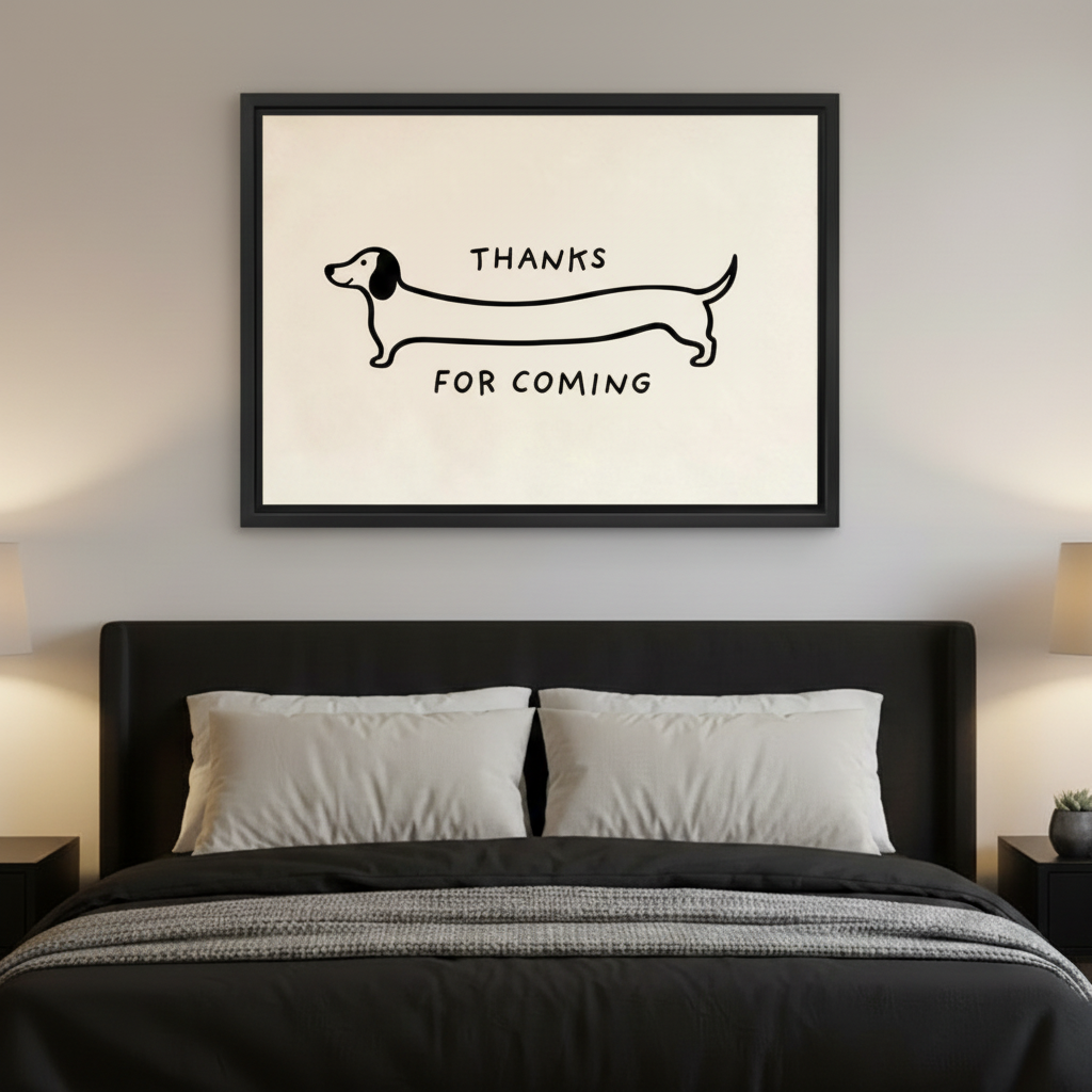 Black framed minimalist dachshund Thanks For Coming line art canvas hung above a dark upholstered bed with white pillows and grey blanket in a moody modern bedroom with warm amber bedside lamps on either side