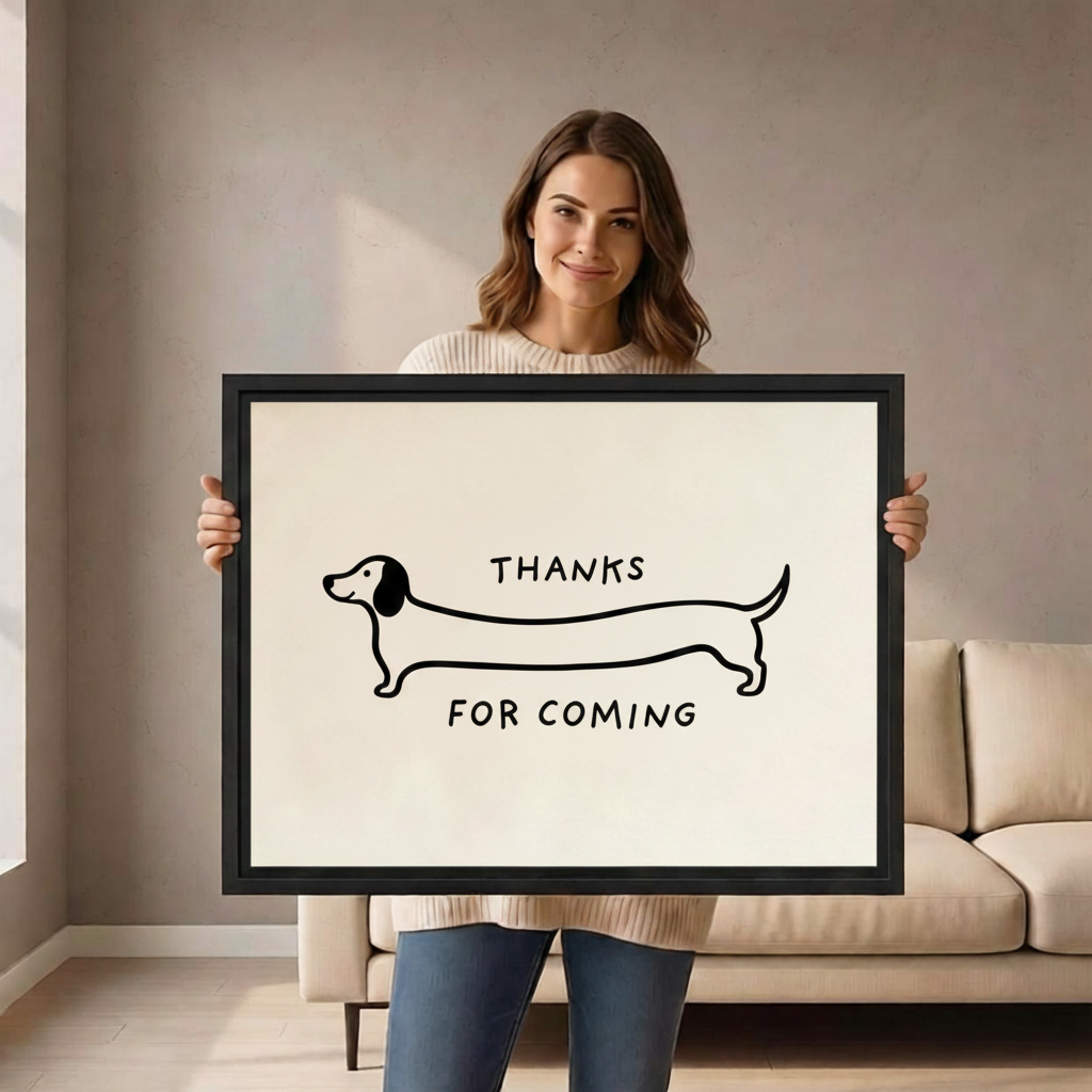 Smiling woman holding a large black-framed canvas print of a minimalist continuous line drawing of a long dachshund with the funny quote Thanks For Coming in hand-lettered text on a clean cream background
