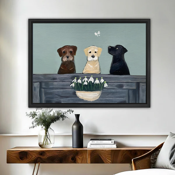 Three Labrador dogs with snowdrop flowers framed canvas wall art in black float frame above wooden console