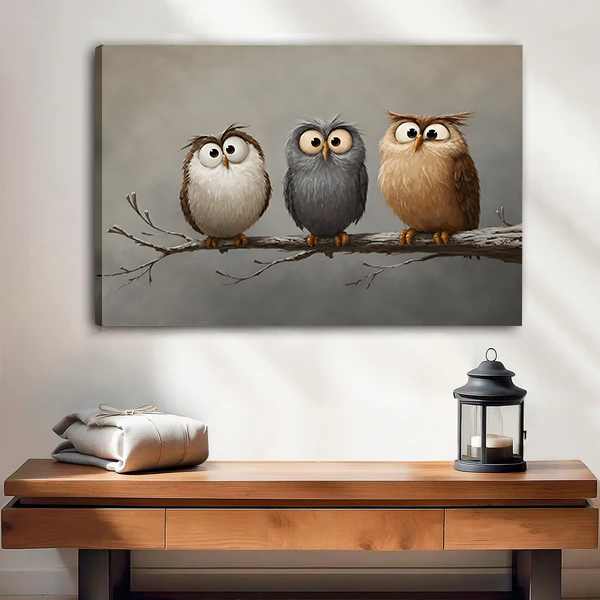 Frameless canvas print of three whimsical owls sitting on a branch, hung above a wooden console table