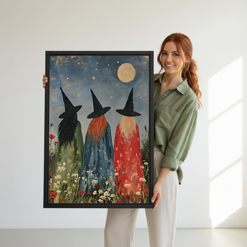 Smiling redhead woman holding large three witches moonlit wildflower folk art black hats full moon star sky daisy poppy black framed canvas wall art size reference in bright white room with natural side light