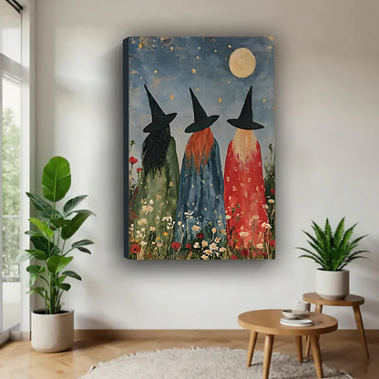 Three witches moonlit wildflower folk art green blue red robes black hats full gold moon star sky wildflower meadow gallery wrap canvas wall art on white wall beside round wood table with monstera and fern