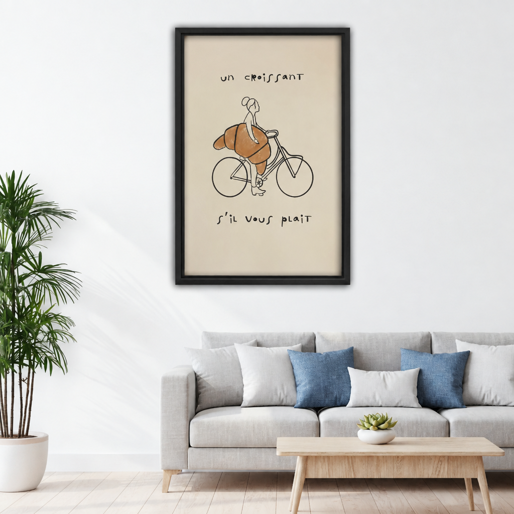 Framed canvas of minimalist French-style line art of a woman cycling with a large golden croissant and handwritten French text on cream background above grey sofa with blue pillows and wood coffee table