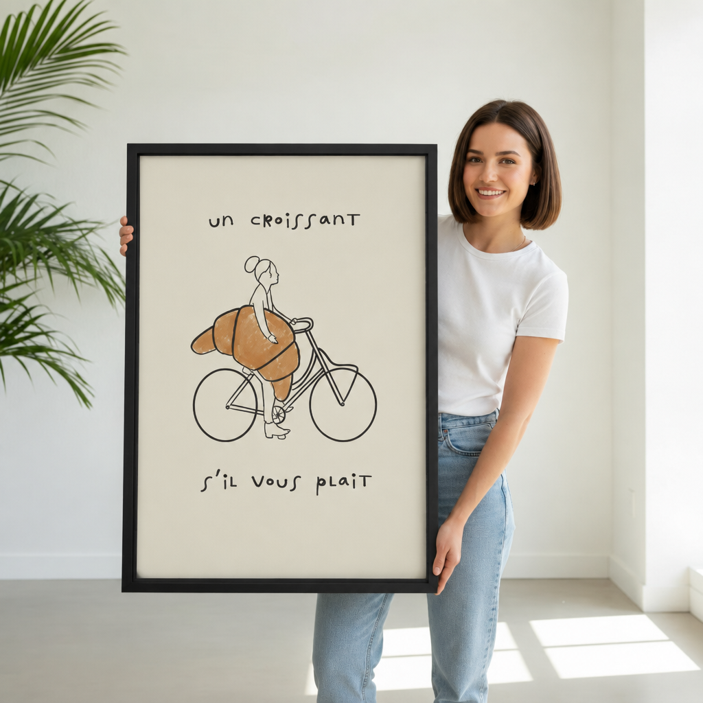 Smiling woman holding large vertical framed canvas of minimalist line art of a woman on a bicycle with a giant golden croissant and French text "un croissant s'il vous plait" on cream background