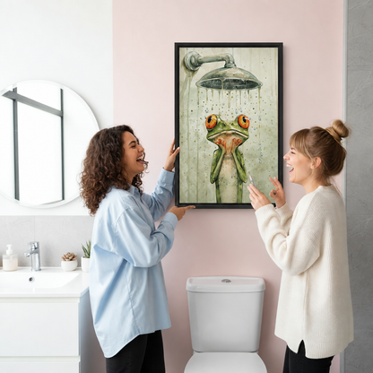 Two women laughing while hanging watercolor shower frog canvas wall art in a pink bathroom