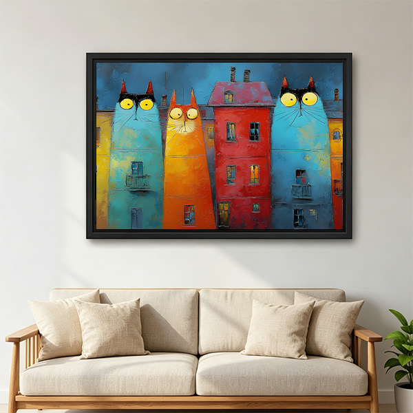 Black-framed whimsical cat buildings canvas wall art featuring three yellow-eyed cat facades displayed above a bed with white pillows.