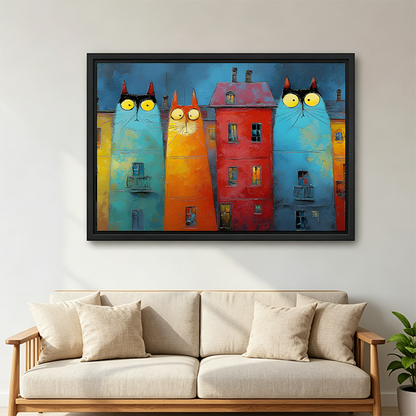 Black-framed whimsical cat buildings canvas wall art featuring three yellow-eyed cat facades displayed above a bed with white pillows.