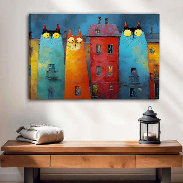 Smiling woman holding black-framed whimsical cat buildings canvas wall art featuring turquoise and orange cats beside a red house.
