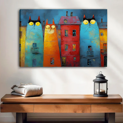 Smiling woman holding black-framed whimsical cat buildings canvas wall art featuring turquoise and orange cats beside a red house.