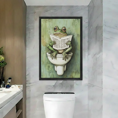 Whimsical frog bathroom canvas wall art in a black frame showing a frog reading a newspaper on a toilet