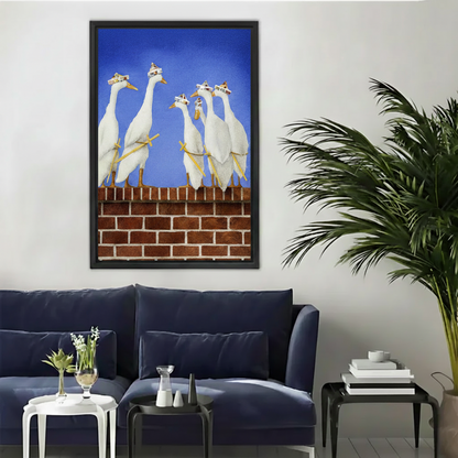 Whimsical oil painting of white geese wearing party hats standing on a red brick wall against a blue sky, displayed as a black framed canvas above a navy sofa