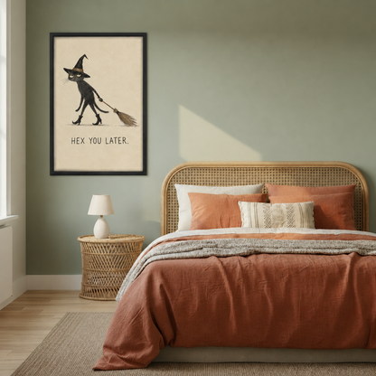 Whimsical witch cat canvas wall art in a black frame beside a bed with rust-colored bedding and woven headboard.