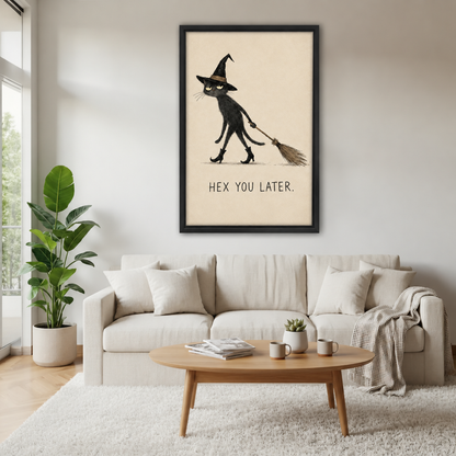 Black-framed whimsical witch cat canvas wall art above a cream sofa, with a wooden coffee table and potted plant.