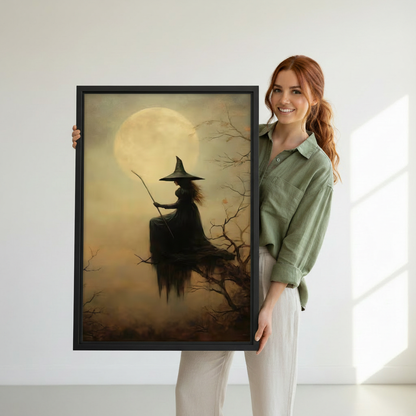 Woman holding vertical framed canvas of gothic witch silhouette in pointed hat on bare branches with broomstick before glowing amber full moon