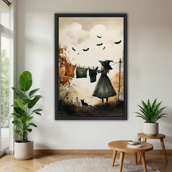 Framed witch laundry day canvas wall art with bats and black cat displayed between indoor plants.