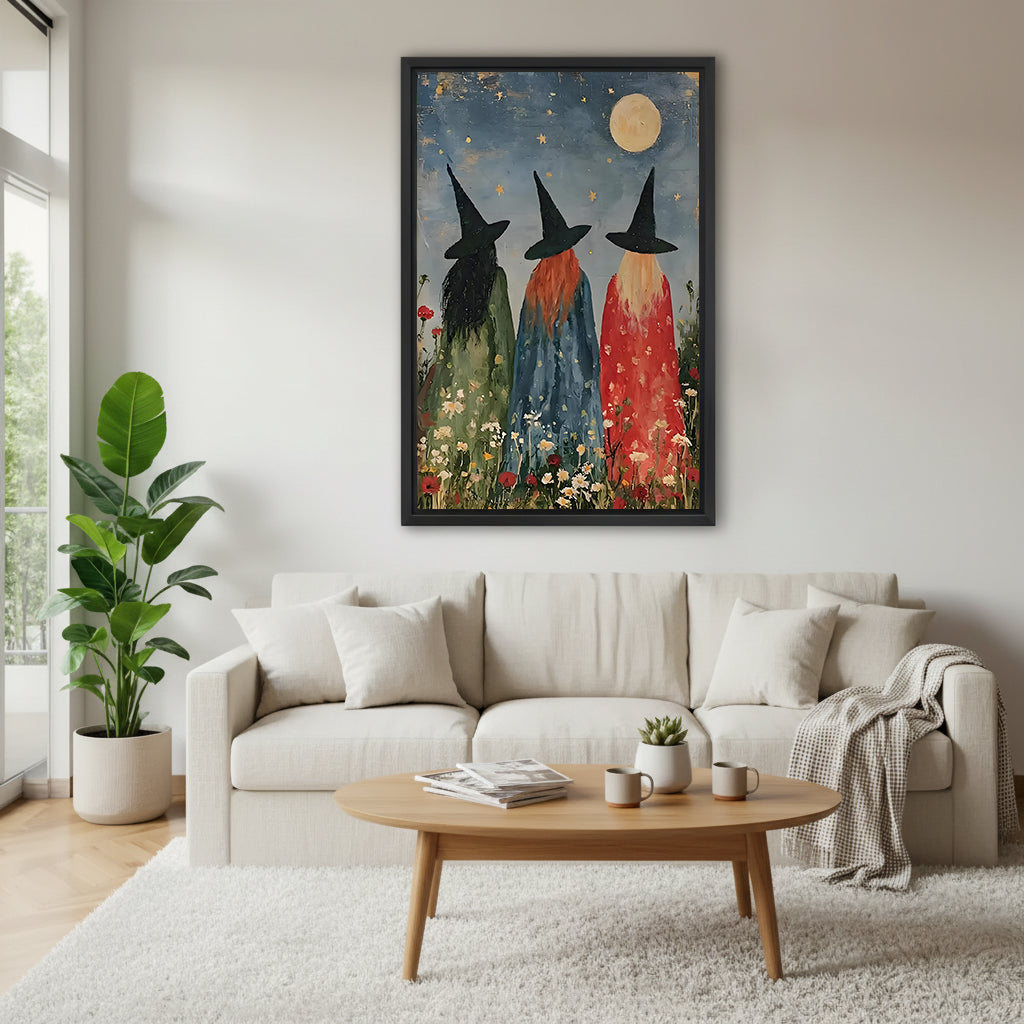 Three witches moonlit wildflower folk art green blue red robes black hats full moon daisy poppy meadow black framed canvas wall art on white wall above cream linen sofa with round wood coffee table and monstera