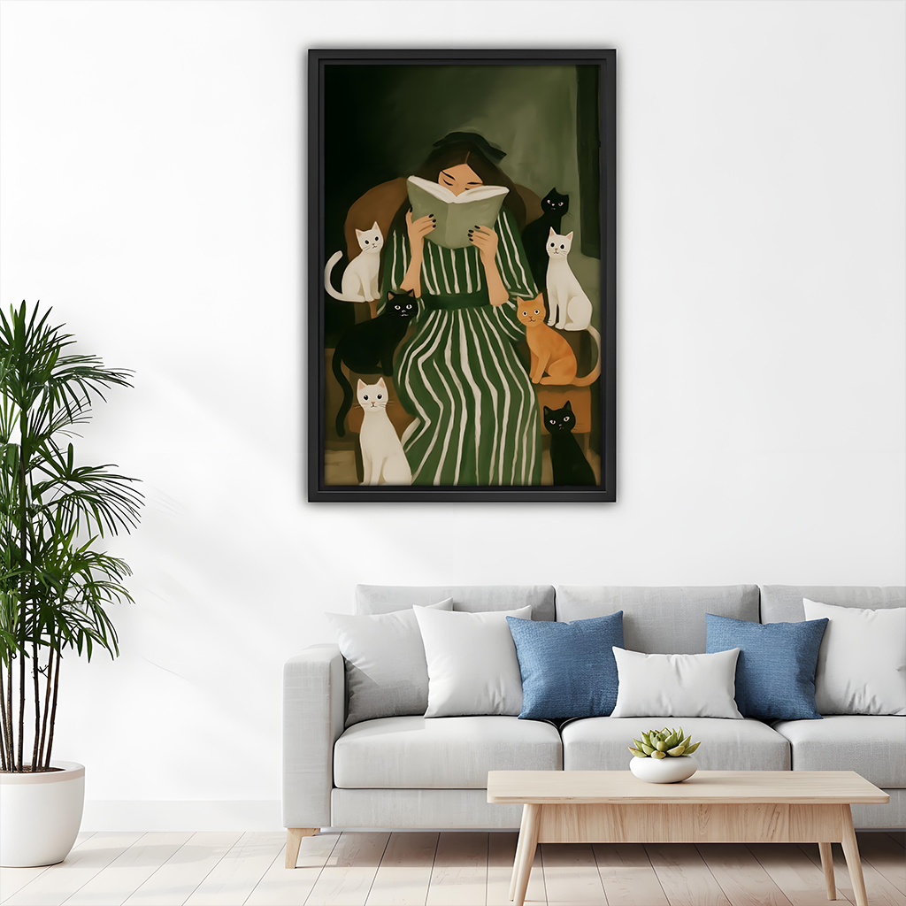 Woman reading with cats canvas wall art in a black frame above a bright living room sofa