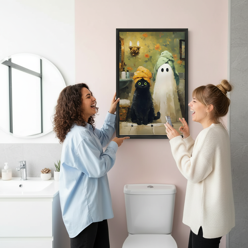 Two women holding framed black cat ghost Halloween canvas wall art in a bright bathroom